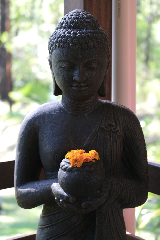 A stone Buddha holding marigold flowers